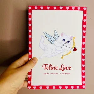 Carte Saint-Valentin A5 Feline Love avec chat blanc ailé en Cupidon tenant arc doré et flèche à cœur rouge, yeux violets, bordure de cœurs roses sur fond rouge, message Cupidon a des ailes et des pattes