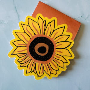 Marque-page magnétique die-cut tournesol jaune et brun posé en lecture sur un livre ouvert