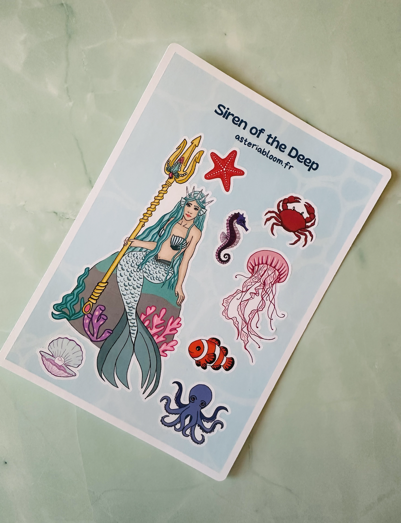 Planche de stickers "Siren of the Deep" 12x17 cm : sirène couronnée, méduse, crabe, pieuvre sur fond bleu aquatique. Papeterie illustrée kawaii. 3,50€.