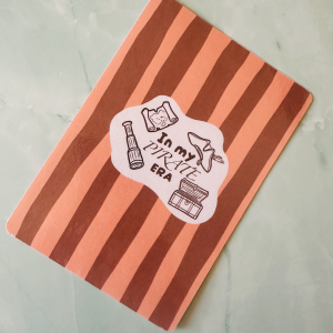 Insert Kindle "In My Pirate Era" avec carte au trésor, longue-vue, chapeau à plume et coffre en doodle brun sur fond rayé terracotta et saumon, posé sur fond marbre vert