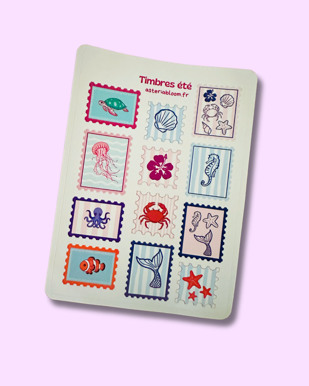 Planche de stickers "Timbres Été" 12x17 cm : 12 stickers façon timbres postaux dentelés aux motifs marins (tortue, méduse, pieuvre, poisson clown, queue de sirène, crabe, hippocampe) sur fond blanc crème, posée sur fond rose lilas