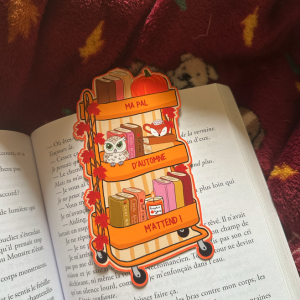 Marque-page die-cut "Ma PAL d'Automne m'attend !" : chariot bibliothèque orange à trois étagères avec livres, citrouille, hibou kawaii et tasse renard, posé ouvert sur un livre